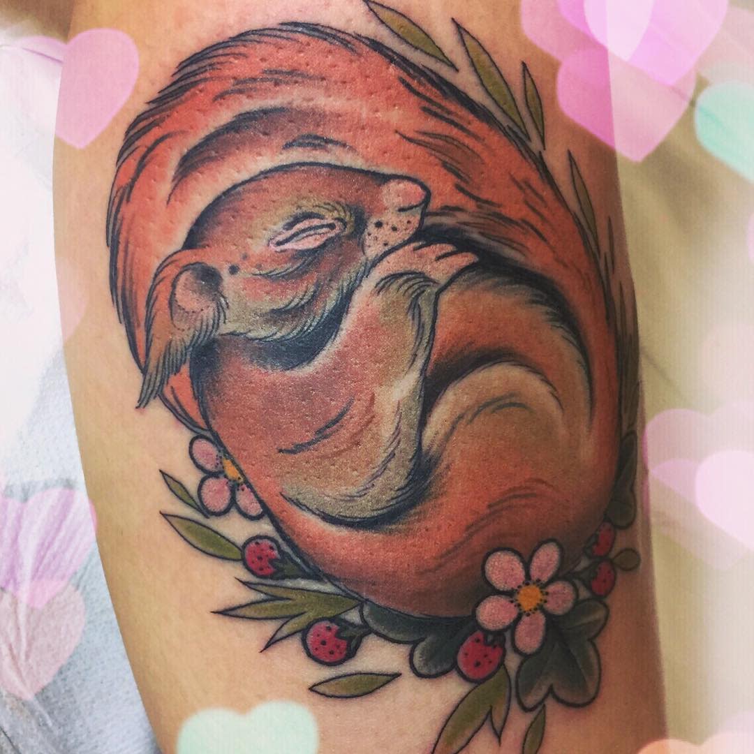 Tattoo of a curled-up sleeping fox surrounded by flowers and berries on skin